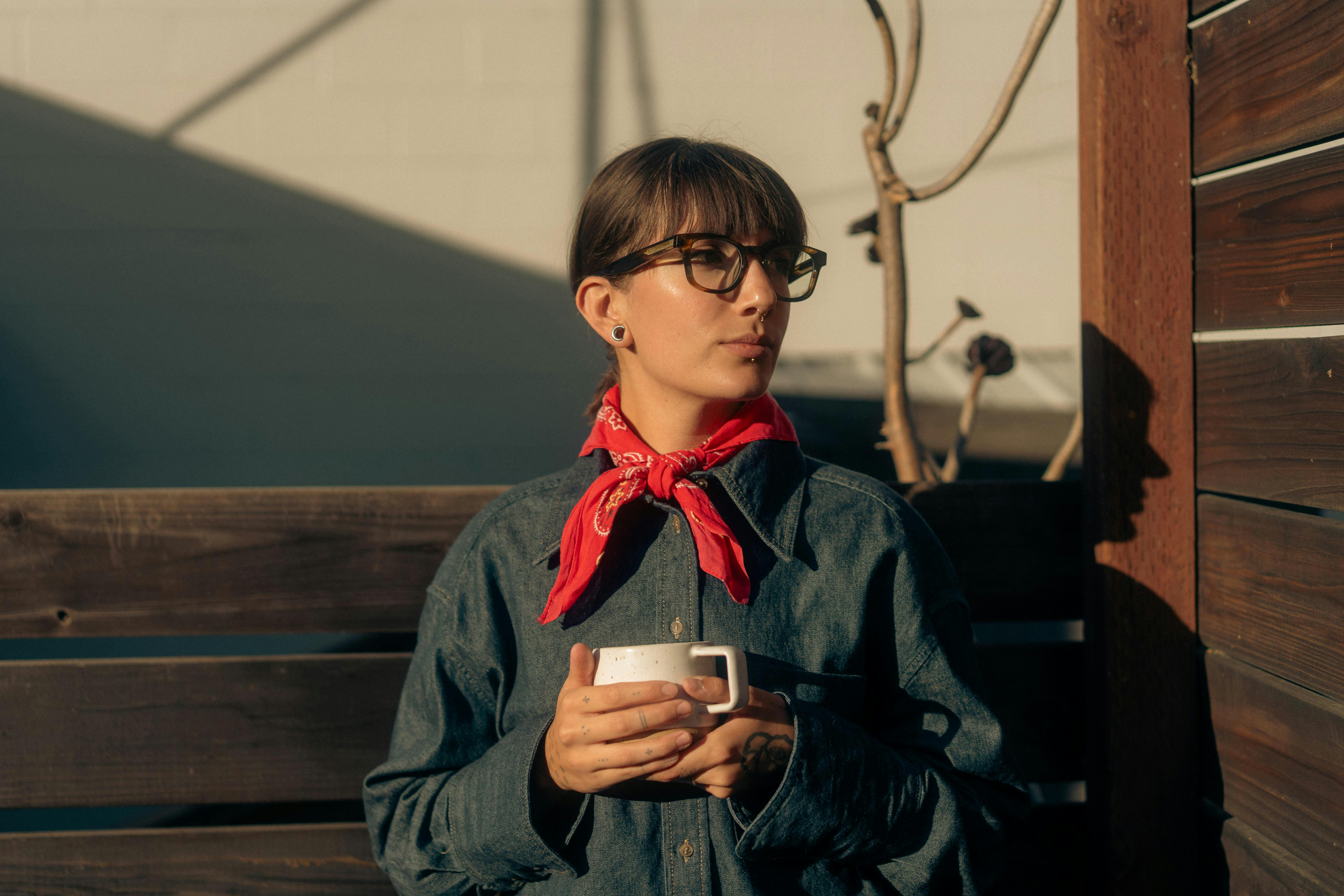 grátis Mulher elegante com bandana vermelha aprecia café ao ar livre sob luz quente. Foto profissional