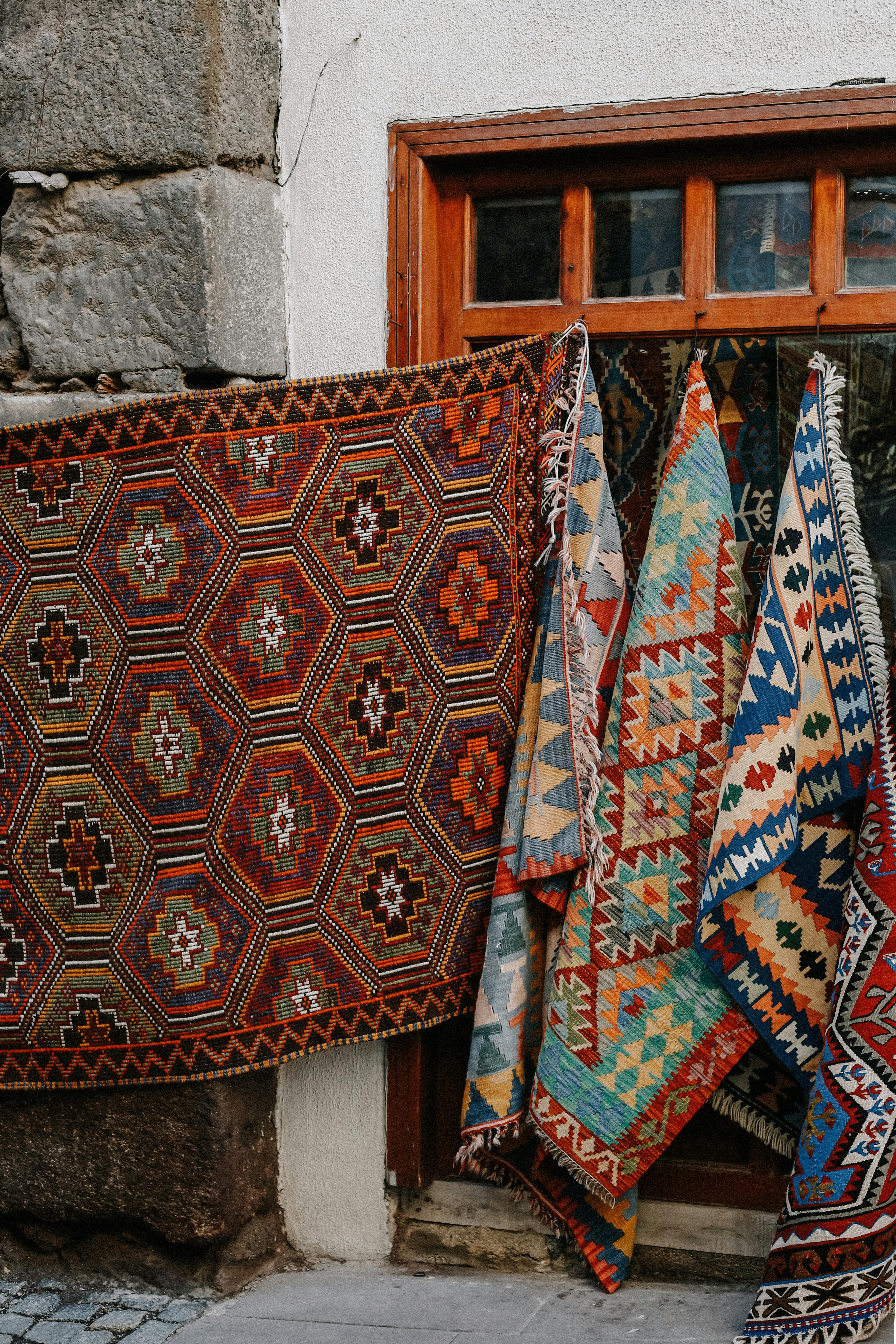 A display of colorful traditional rugs with intricate patterns hanging outdoors.