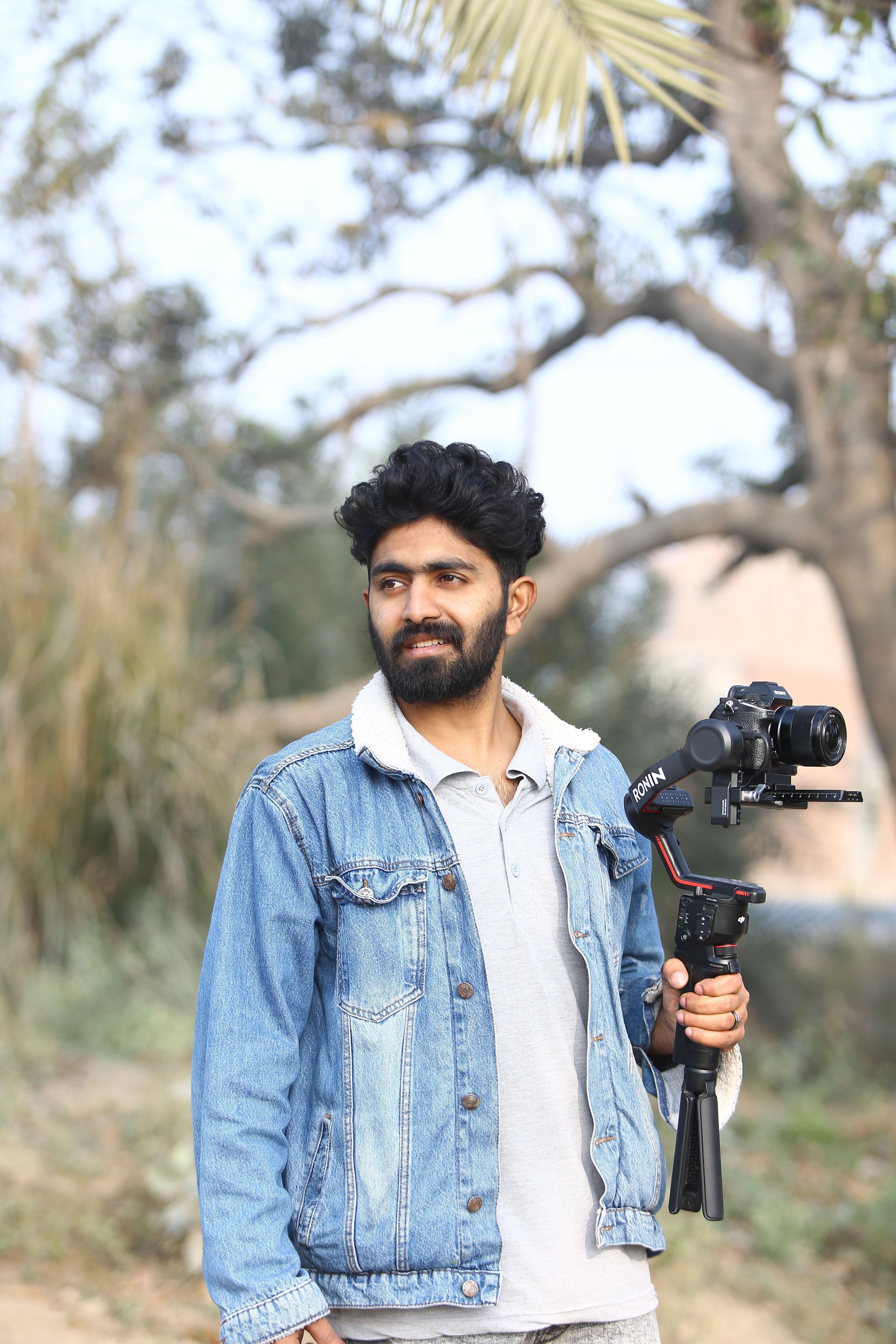 A young adult male videographer filming outdoors with a camera stabilizer in Lahore, Pakistan.