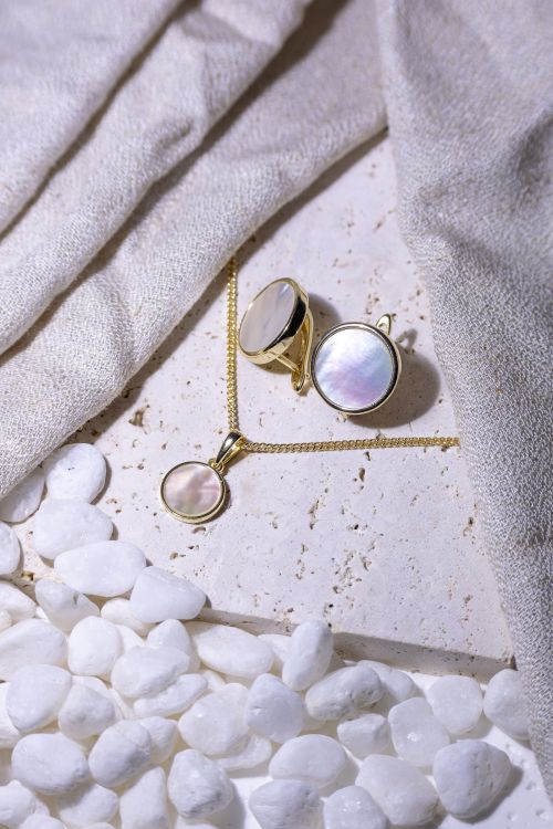 Free Gold-plated mother of pearl jewelry displayed elegantly on white stones with a soft fabric backdrop. Stock Photo