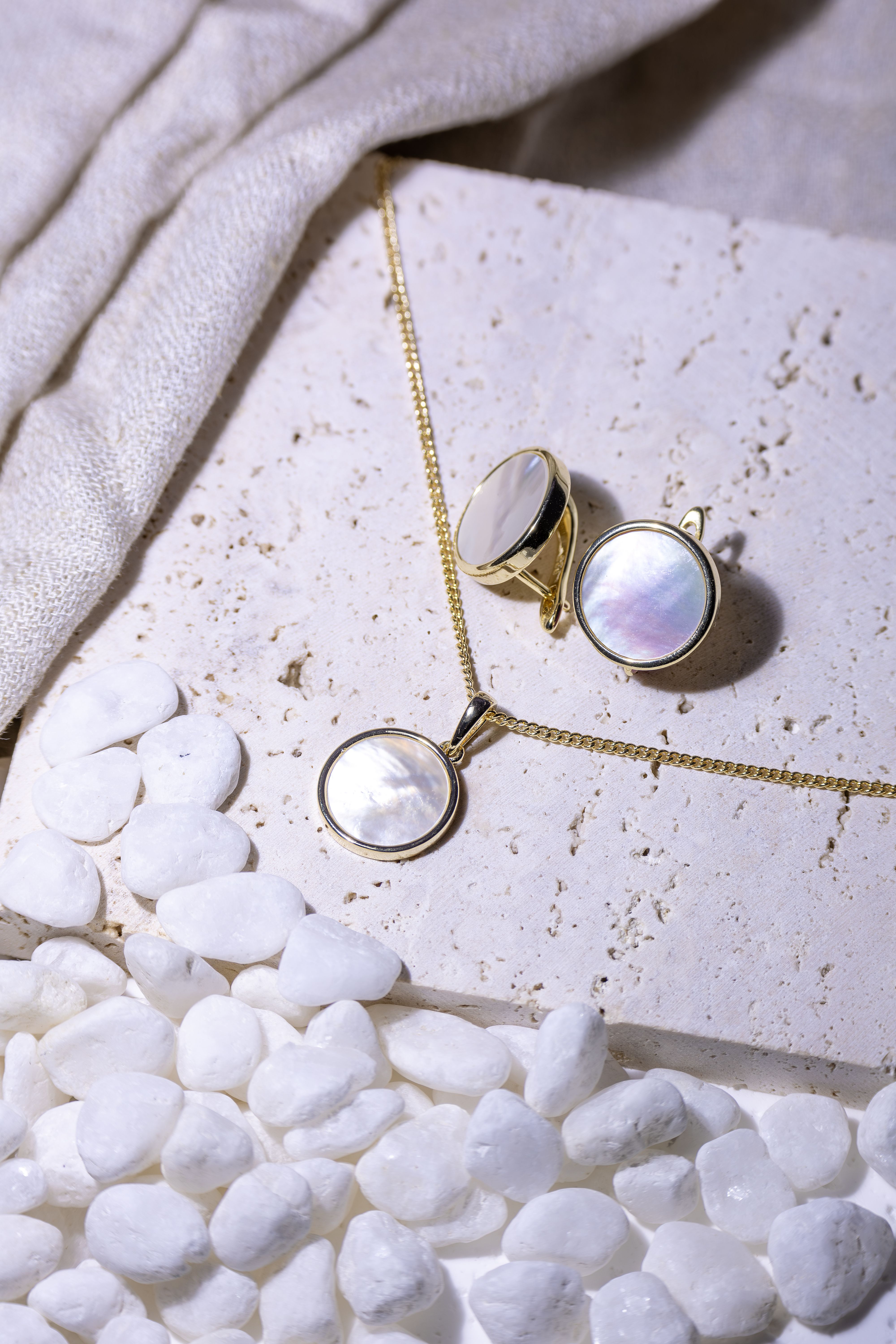 Close-up of elegant mother of pearl jewelry on marble surface with white pebbles, showcasing sophistication.