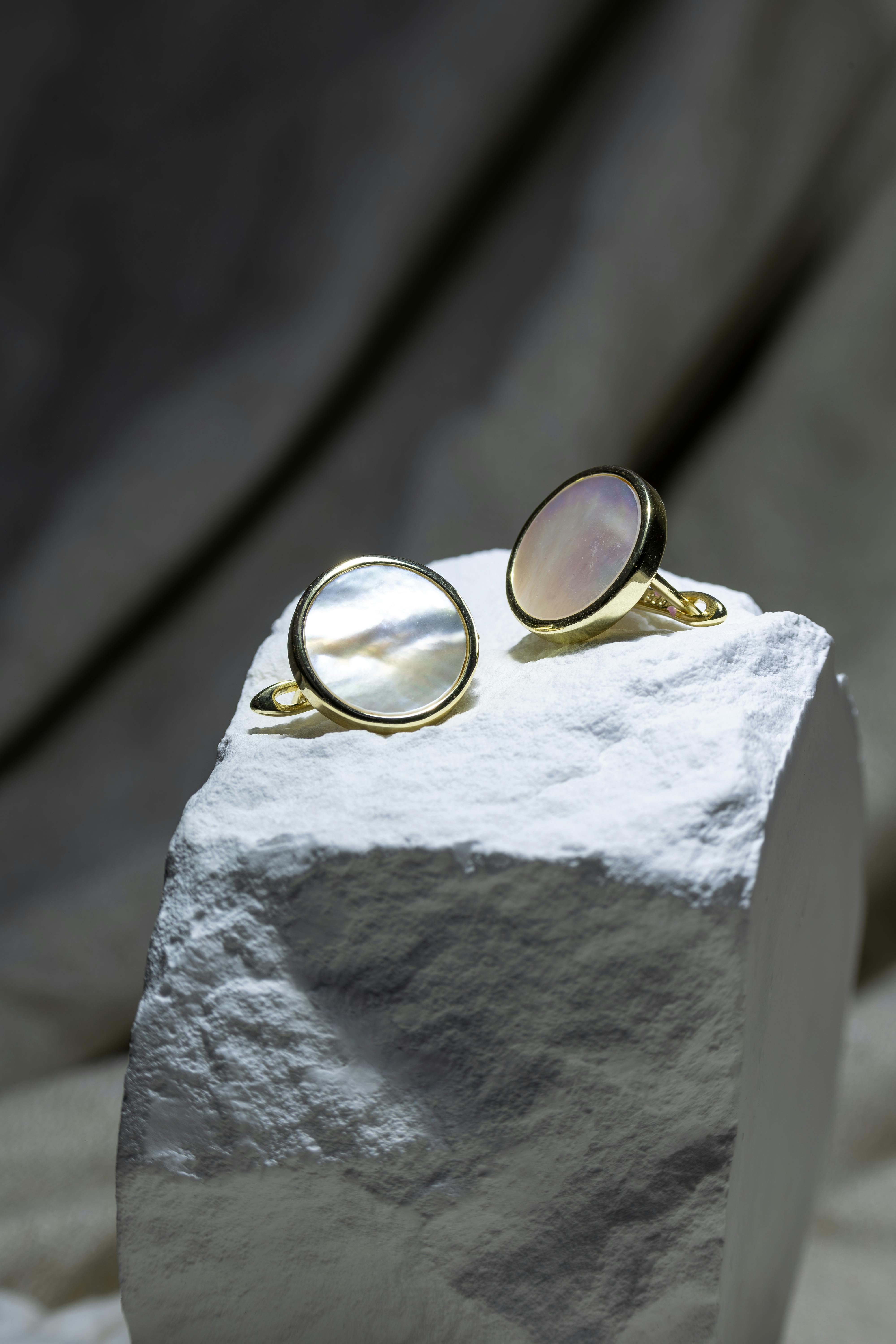 Chic gold rings with mother of pearl inlay on textured stone, suitable for luxury fashion shoots.