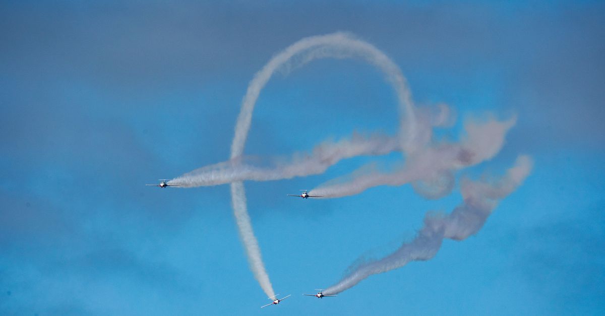 Aerobatic planes perform impressive stunts with smoke trails against a vibrant blue sky.