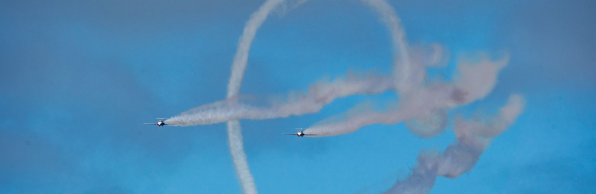 Aerobatic planes perform impressive stunts with smoke trails against a vibrant blue sky.