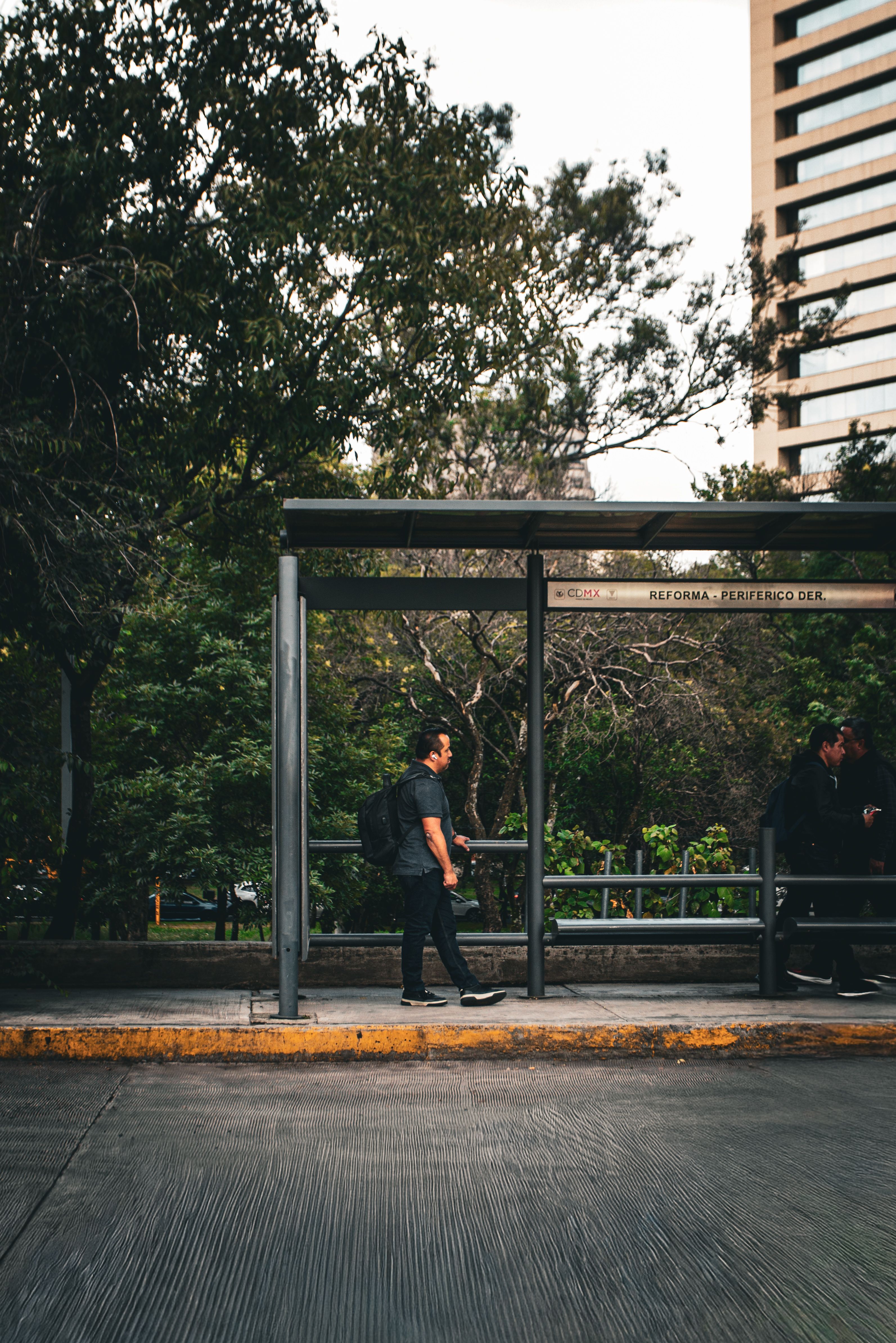 Man waiting at a bus stop in Mexico City with an urban and green backdrop
