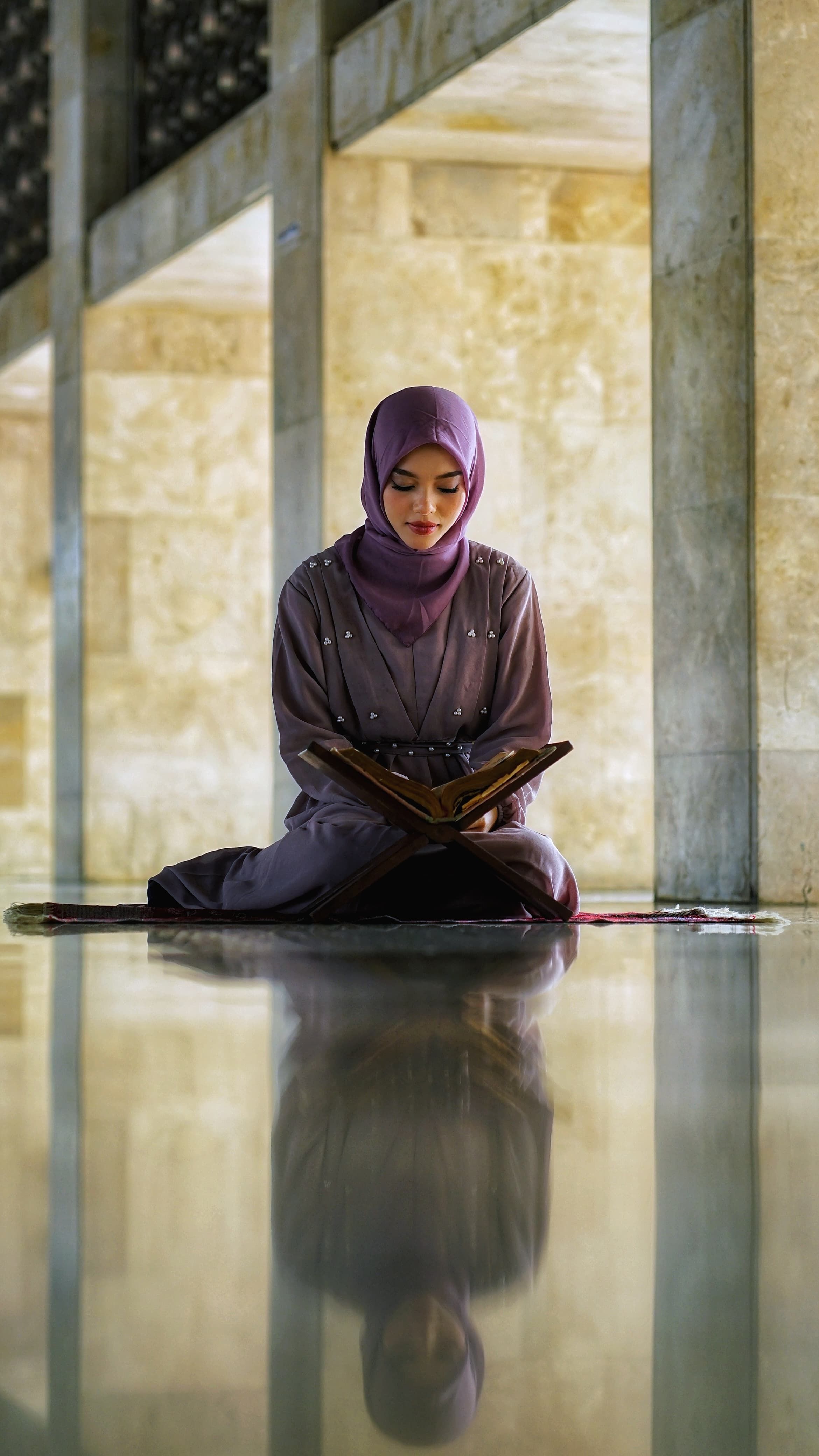 A woman in a purple hijab reading the Quran in a mosque in Jakarta, Indonesia.