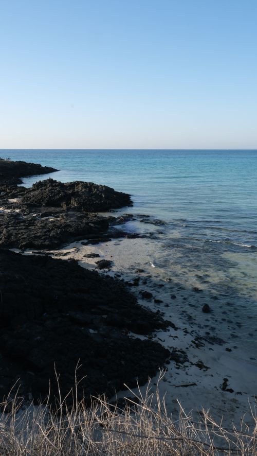 Free Serene coastal landscape of Jeju Island featuring volcanic rocks and clear blue water. Stock Photo
