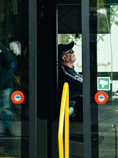 Free Side view of a man relaxing inside a city bus, wearing sunglasses and cap, adding to urban theme. Stock Photo