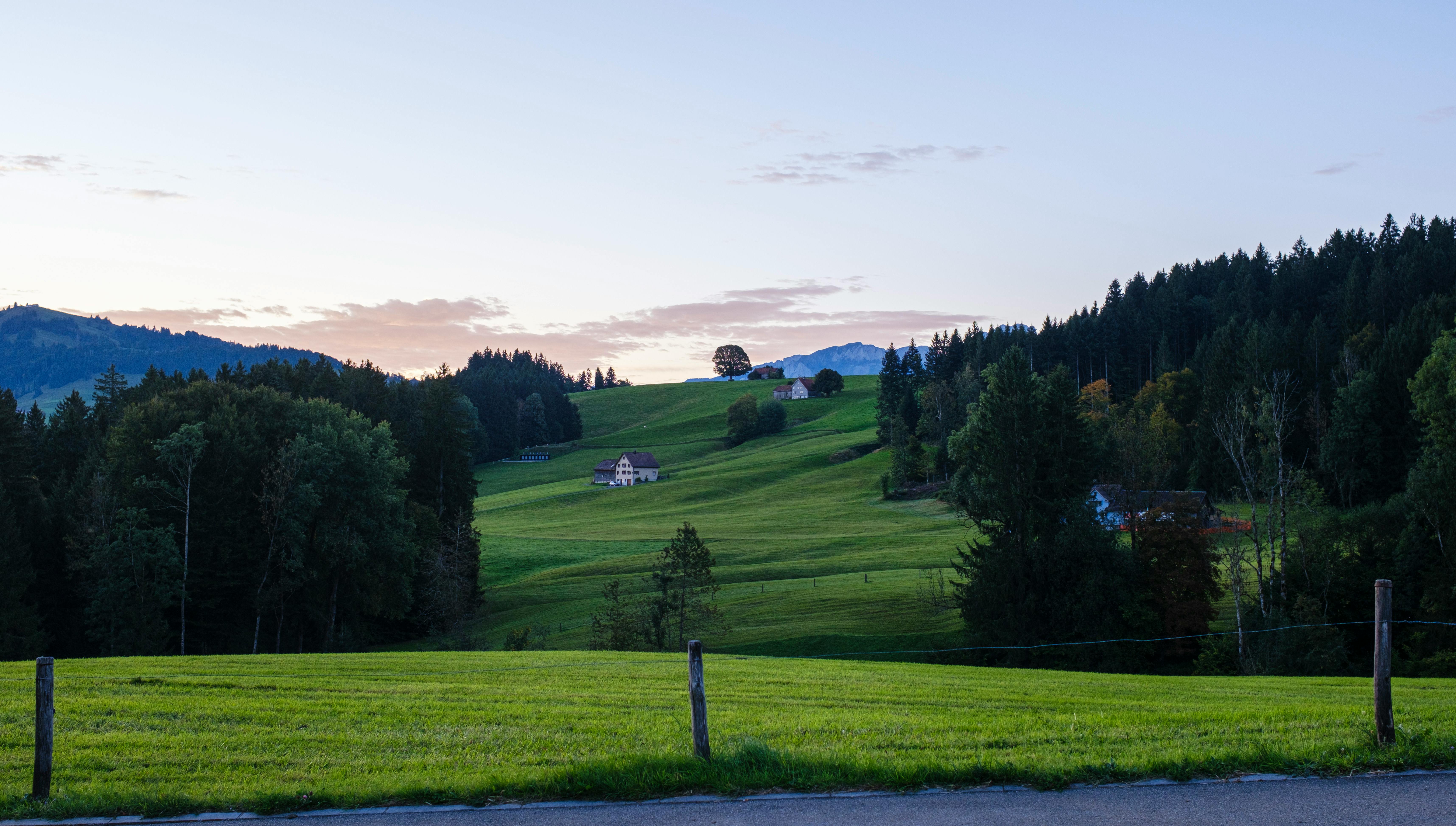 Peaceful dusk landscape in Appenzell Ausserrhoden, Switzerland with lush green meadows and distant mountains.