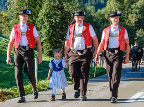 People in traditional Appenzell costumes walking on a sunny day in Switzerland's countryside.