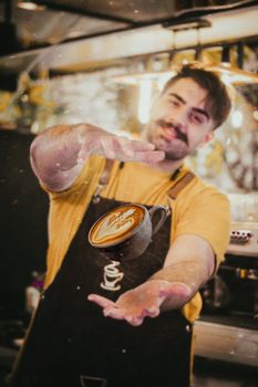 A creative barista showcasing latte art in a lively Kermanshah café setting.