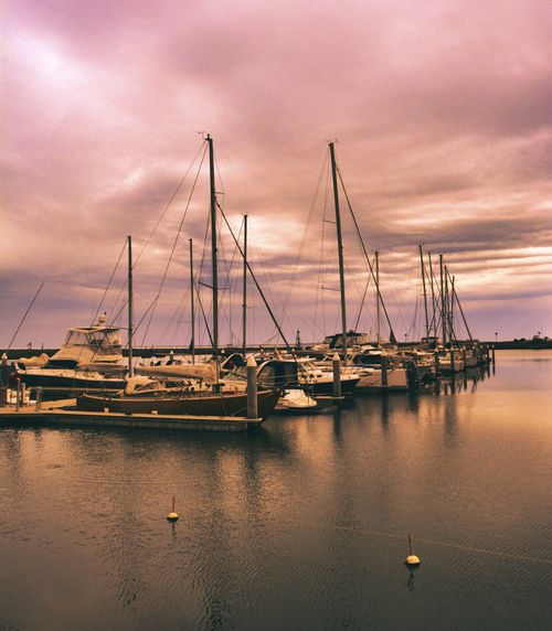 Free Serene view of yachts docked at a marina under a dramatic sunset sky. Stock Photo