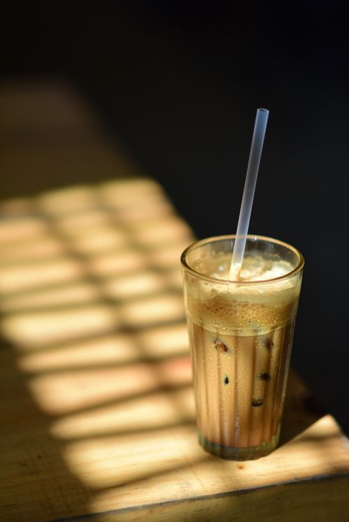 Free A glass of iced coffee with a straw, highlighted by sunlight on a wooden surface. Stock Photo