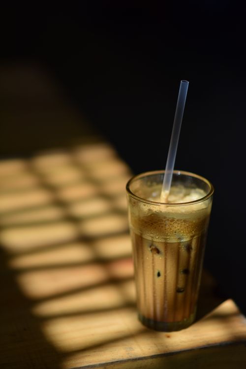 Free Refreshing iced coffee in a glass with straw, captured amidst playful sunlight and shadows. Stock Photo