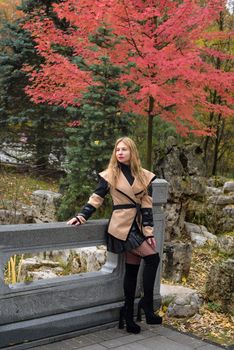 Stylish woman posing by vibrant red maple trees, showcasing fall fashion.
