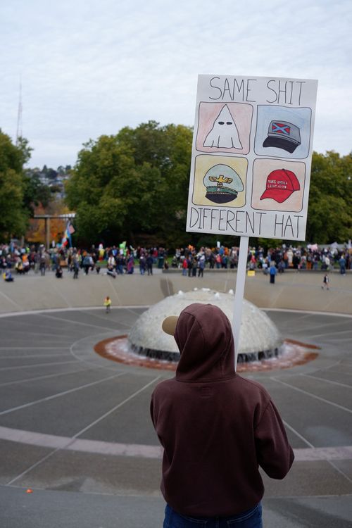 Free A protester holds a satirical sign during an outdoor gathering by a fountain. Stock Photo