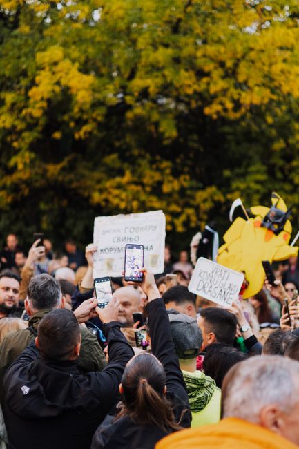 Crowd at a protest in Belgrade holding signs and smartphones during fall.