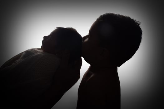 A touching silhouette of a child kissing a baby sibling, symbolizing love and family bonds.