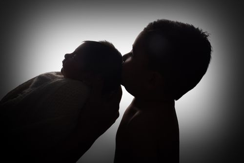 Free A touching silhouette of a child kissing a baby sibling, symbolizing love and family bonds. Stock Photo