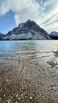 Breathtaking view of a mountain with a rocky shoreline by a serene lake under a cloudy sky.