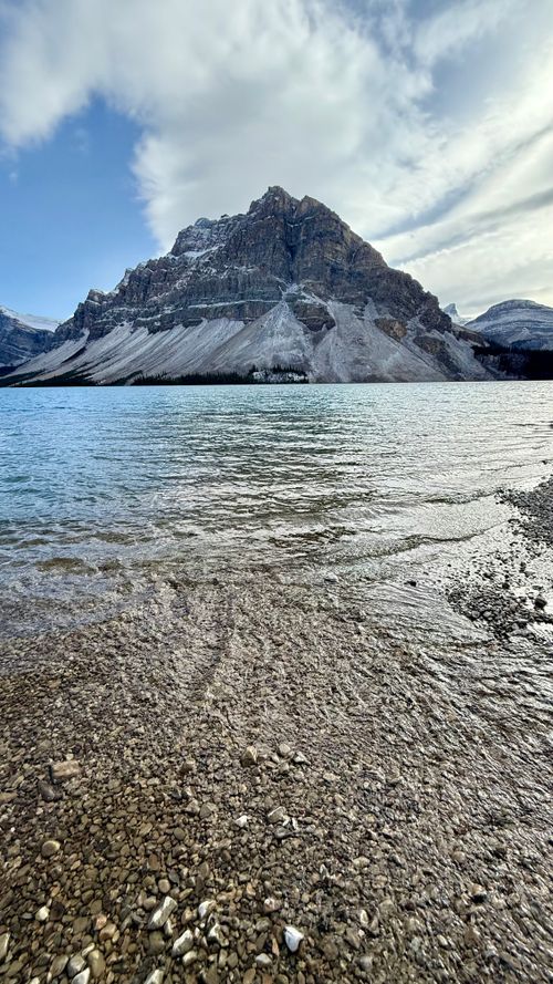 Free Breathtaking view of a mountain with a rocky shoreline by a serene lake under a cloudy sky. Stock Photo
