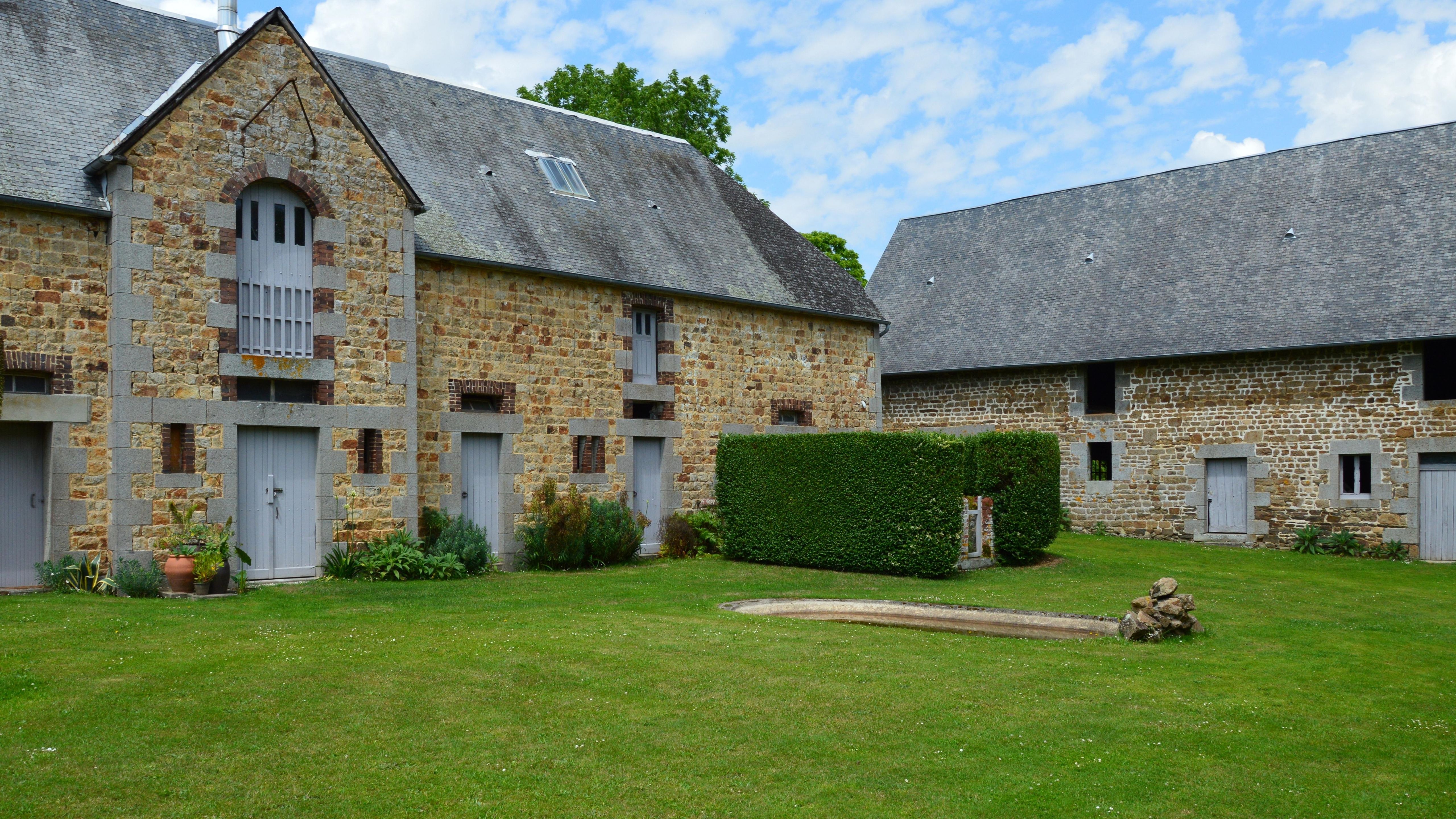 Corps de ferme en pierre et toits d'ardoise autour d'une cour enherbée.