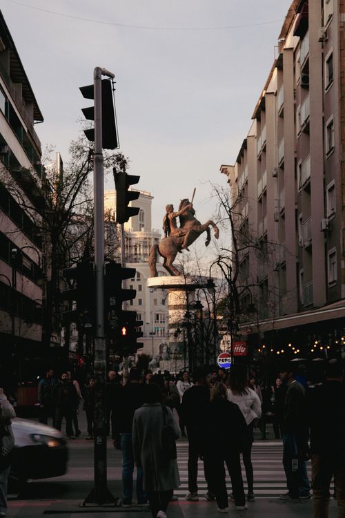 Free Street view of Skopje featuring the famous Warrior on Horse statue during evening hours with bustling crowd. Stock Photo