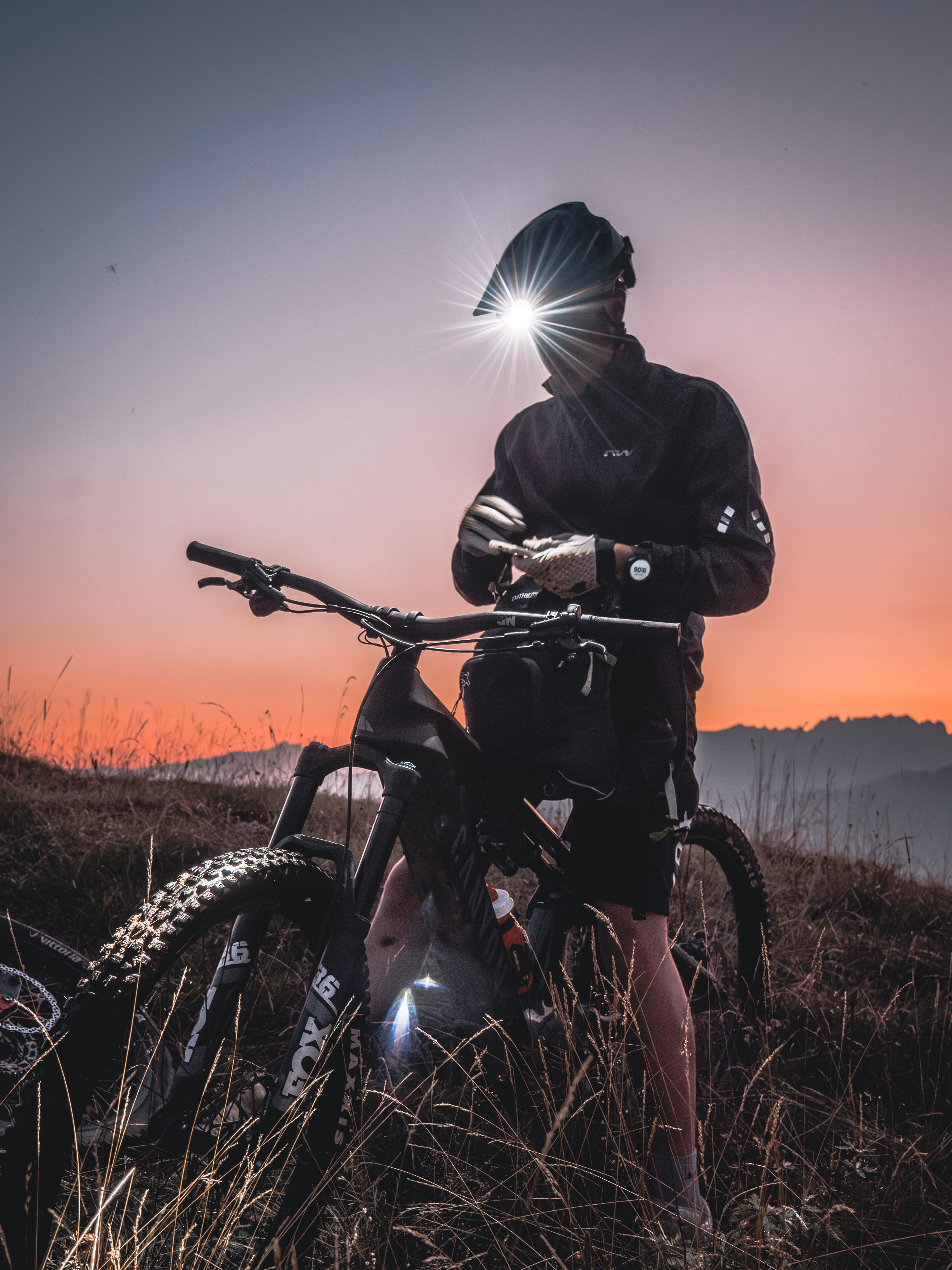Mountain biker prepares for night ride at sunset with a headlamp on a scenic trail.