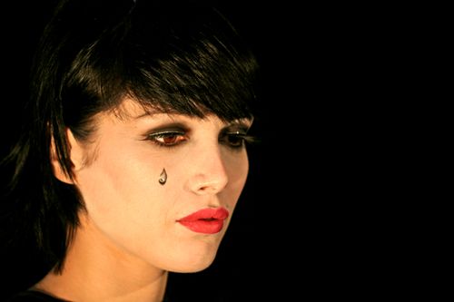 Free Close-up portrait of a woman with dramatic makeup and a teardrop on her cheek against a black background. Stock Photo