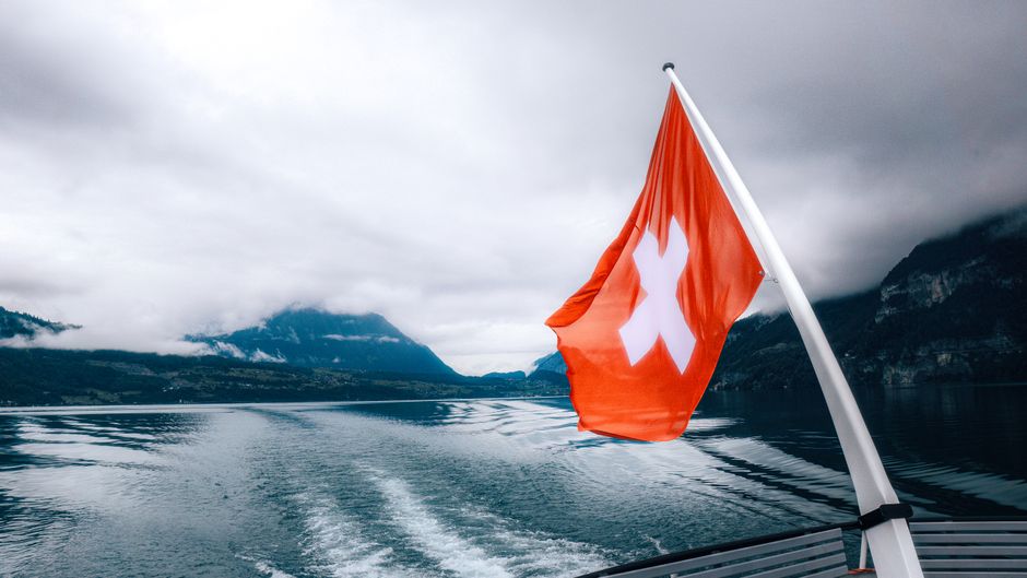 A serene boat ride with a Swiss flag waving, surrounded by stunning mountain views.