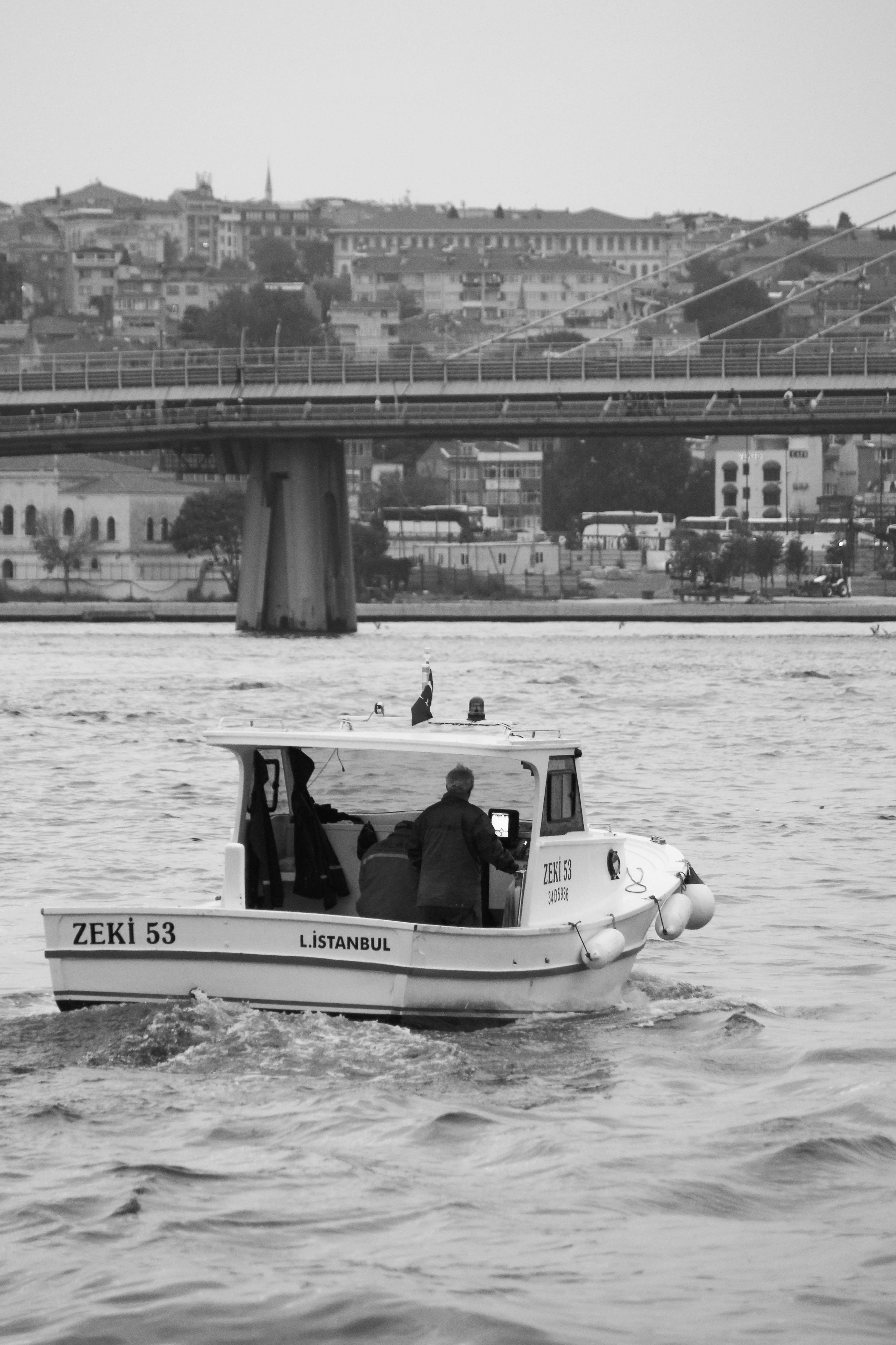 Black and white image of a small boat navigating the waters of Istanbul with the city skyline in background.