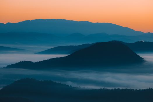 A breathtaking view of fog rolling over the Slovenian mountains at sunrise creating a serene atmosphere.