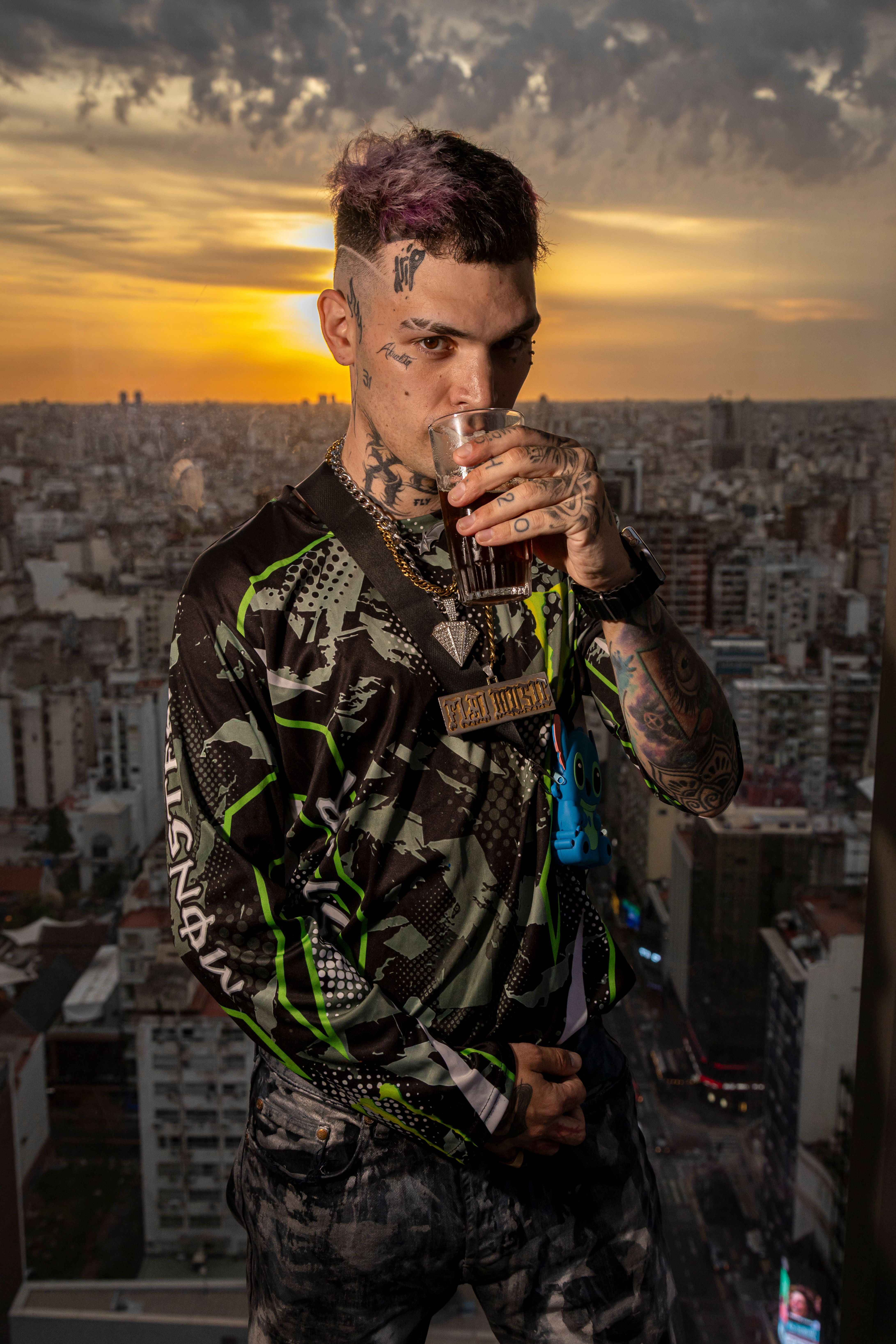 A tattooed man with trendy style sipping a drink at sunset overlooking Buenos Aires.