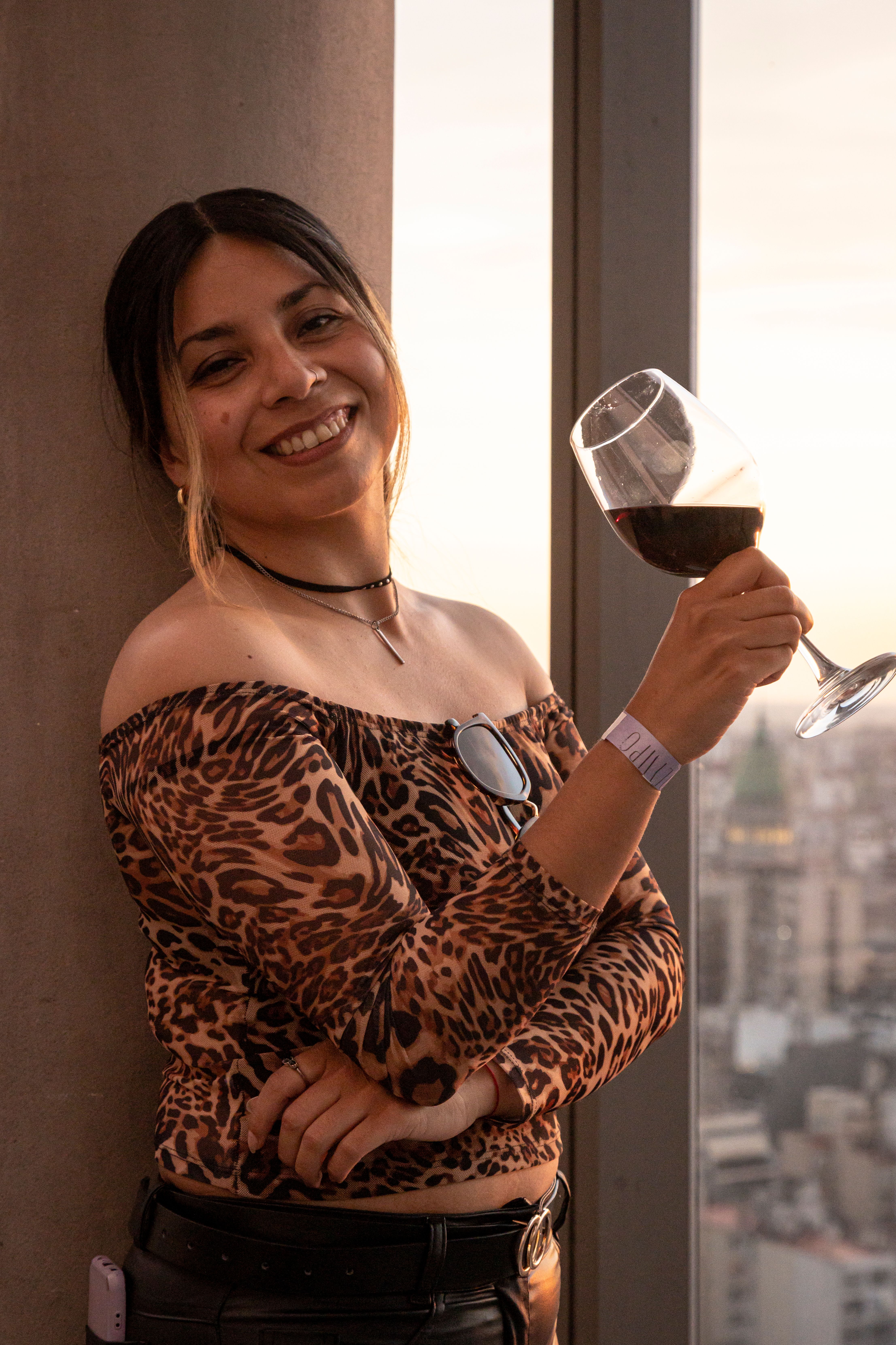 A cheerful woman in a leopard print top holds a glass of wine at sunset in Buenos Aires.