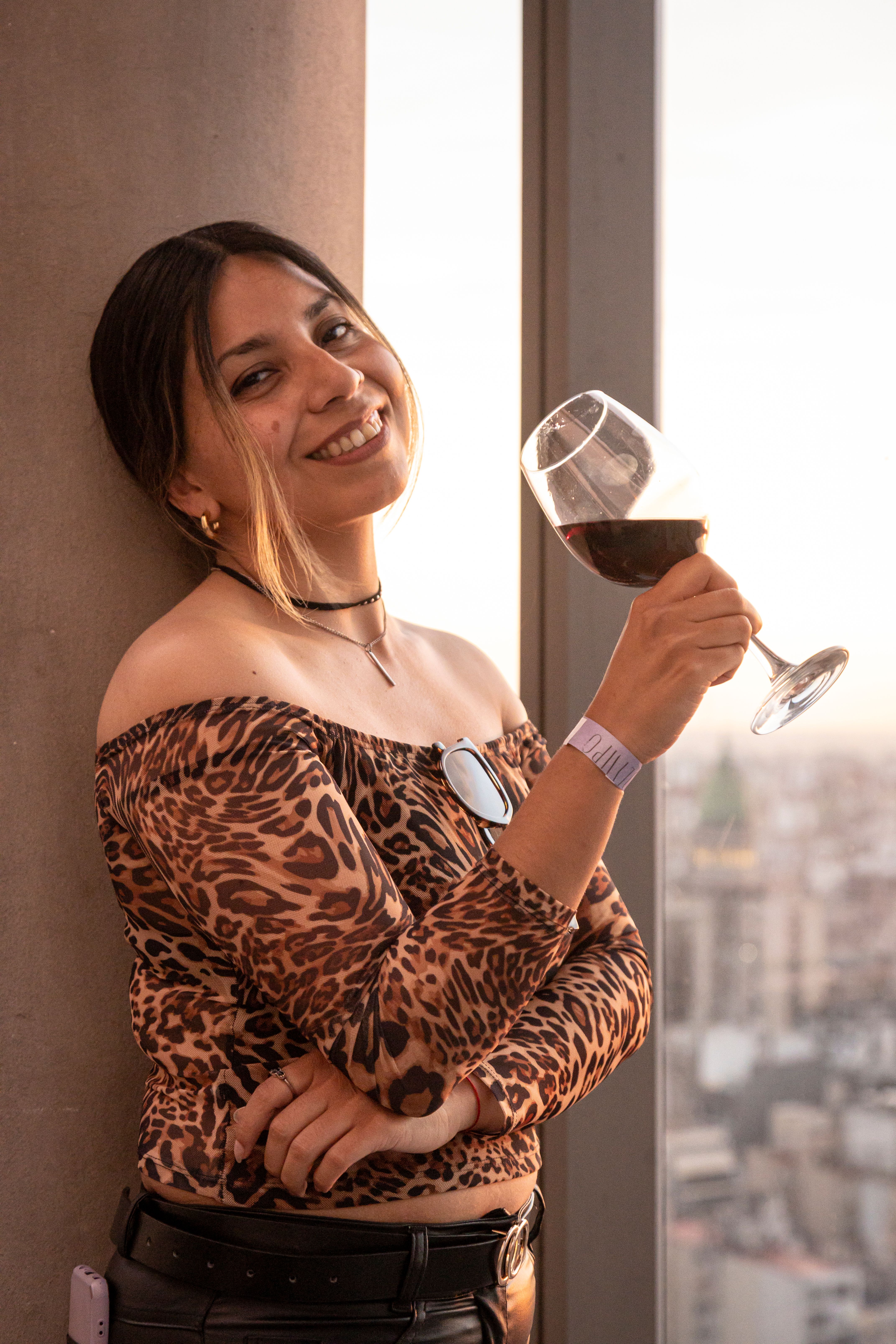 Stylish woman in leopard print top enjoying wine with a sunset view in Buenos Aires.