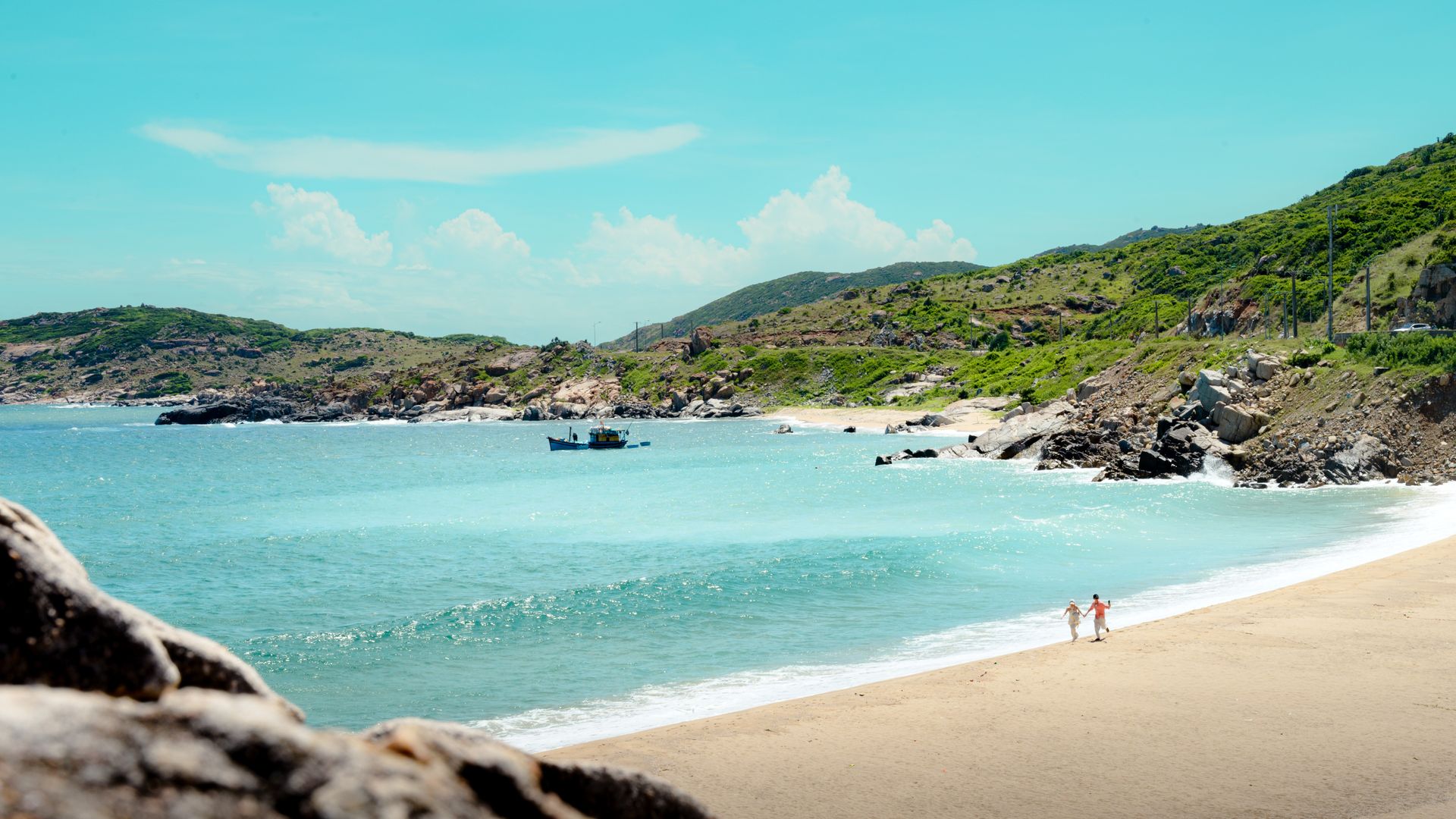 Stunning beach landscape in Ninh Thuận, Vietnam with a couple walking by the shore under a clear blue sky.