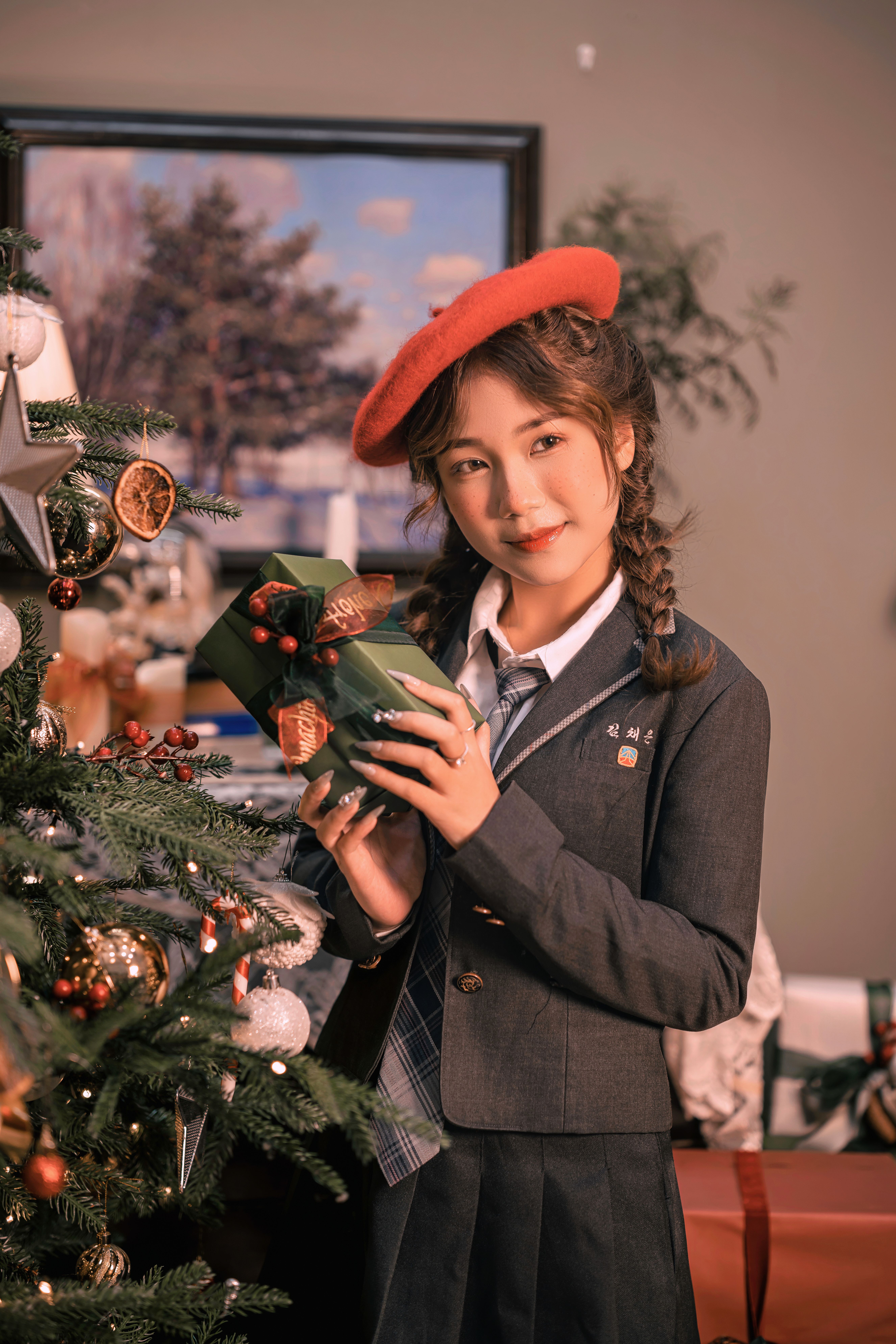 Young woman in school uniform holding a gift by a decorated Christmas tree.