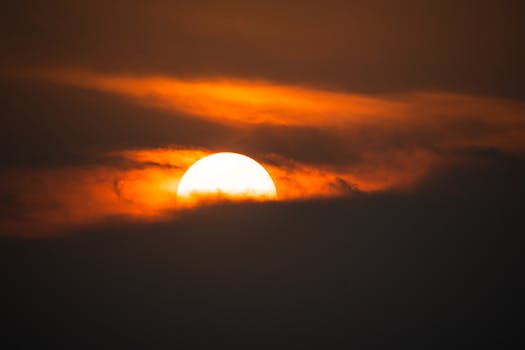 A vibrant sunset with the sun partially obscured by dark clouds, creating a dramatic and vivid sky.