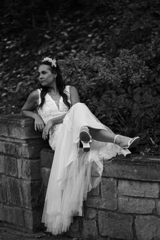 A stylish black and white portrait of a bride relaxing outdoors in her elegant wedding dress.