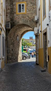 A picturesque view through a stone archway in a historic town with people and classic architecture in the background.