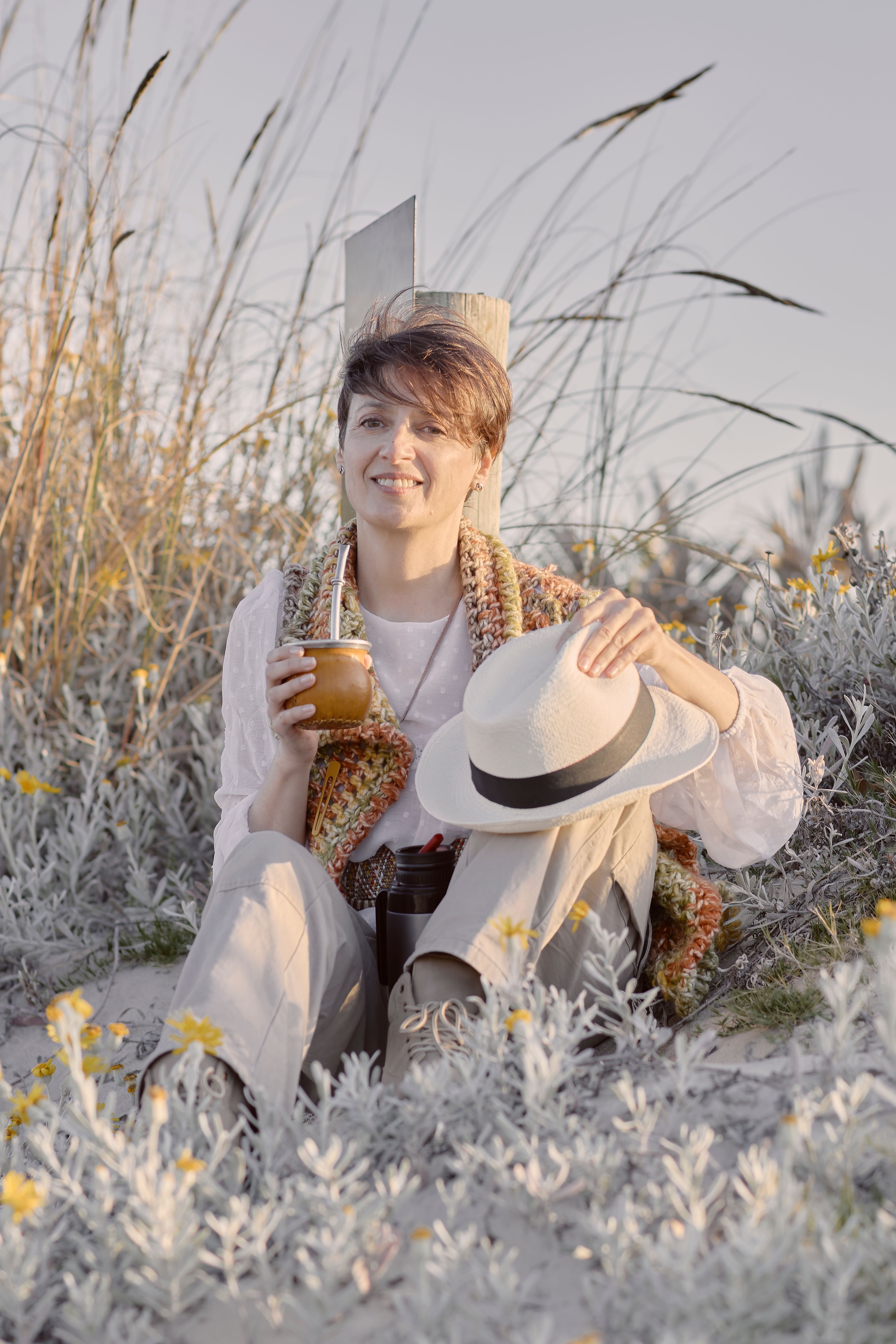 Woman enjoying a peaceful beach day in Montevideo, sipping mate and holding a hat.