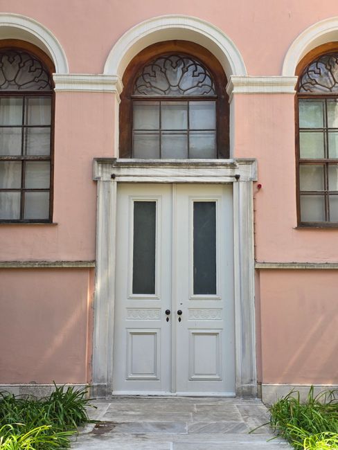 A classic white door set in a pink facade, flanked by windows in Türkiye. Architectural elegance on display.