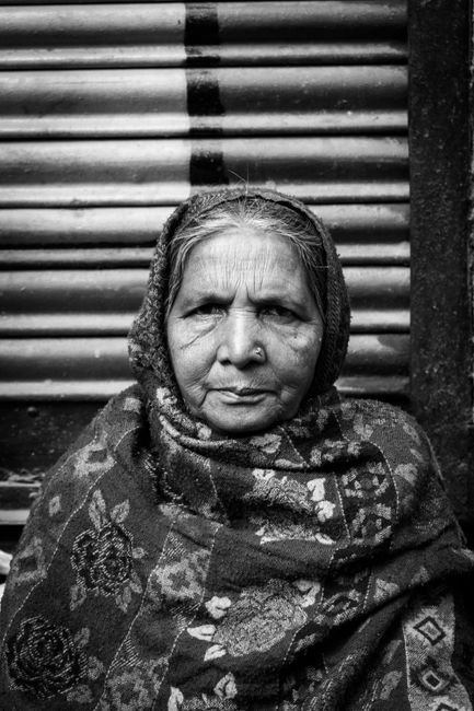 Black and white portrait of an elderly woman with a headscarf and serious expression.