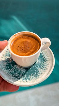 A rich espresso served in a ceramic cup with artistic saucer, captured outdoors in daylight.