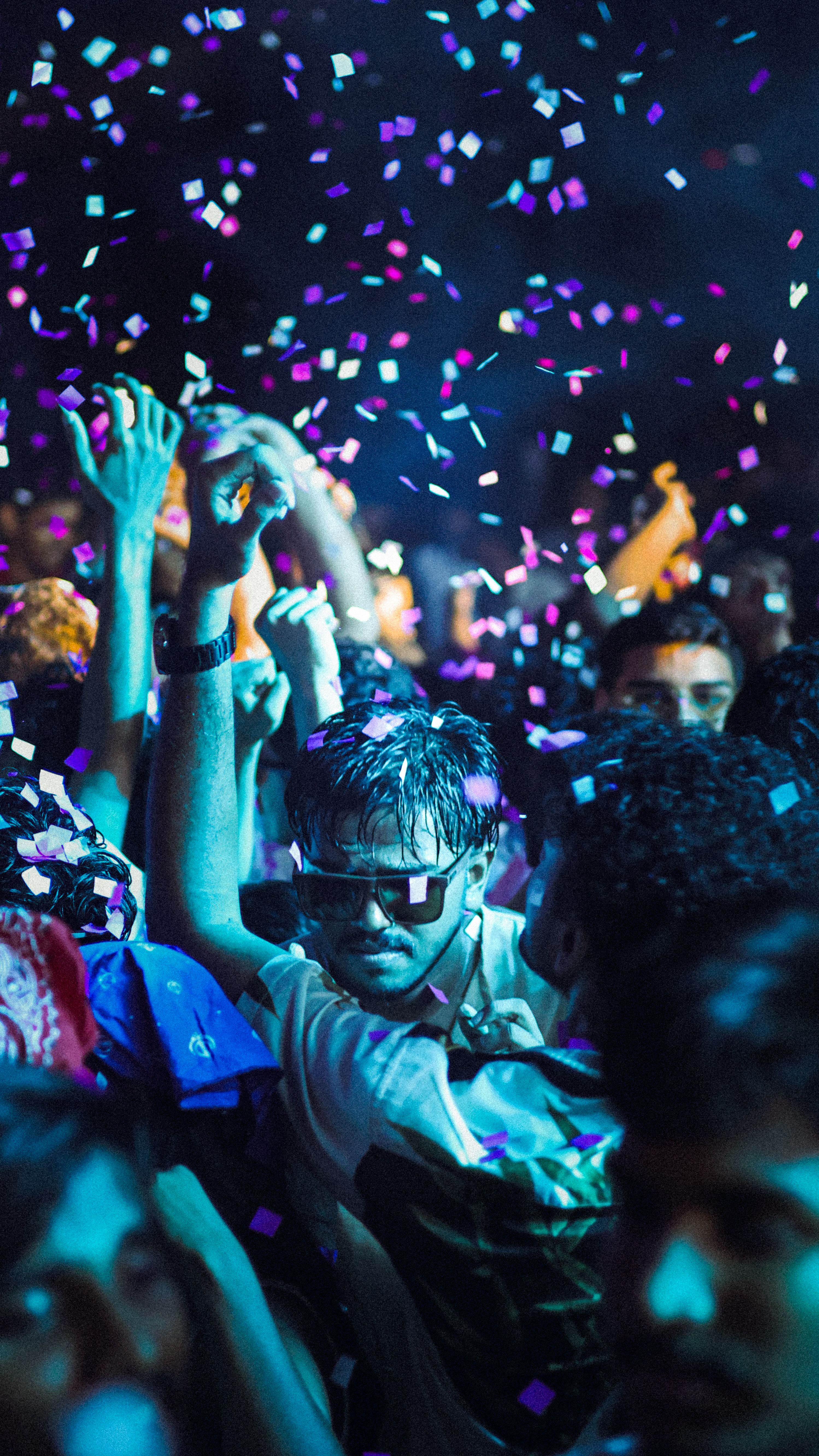 A lively night party scene with people dancing amidst colorful confetti under bright lights.