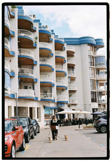 Urban scene of a multi-story hotel with parked cars and people walking dogs.