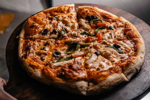 Free Close-up of a freshly-baked vegetable pizza with olives, peppers, and mushrooms on a wooden board. Stock Photo