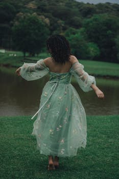 A woman in a flowing green dress gracefully dances near a serene lake surrounded by lush greenery.