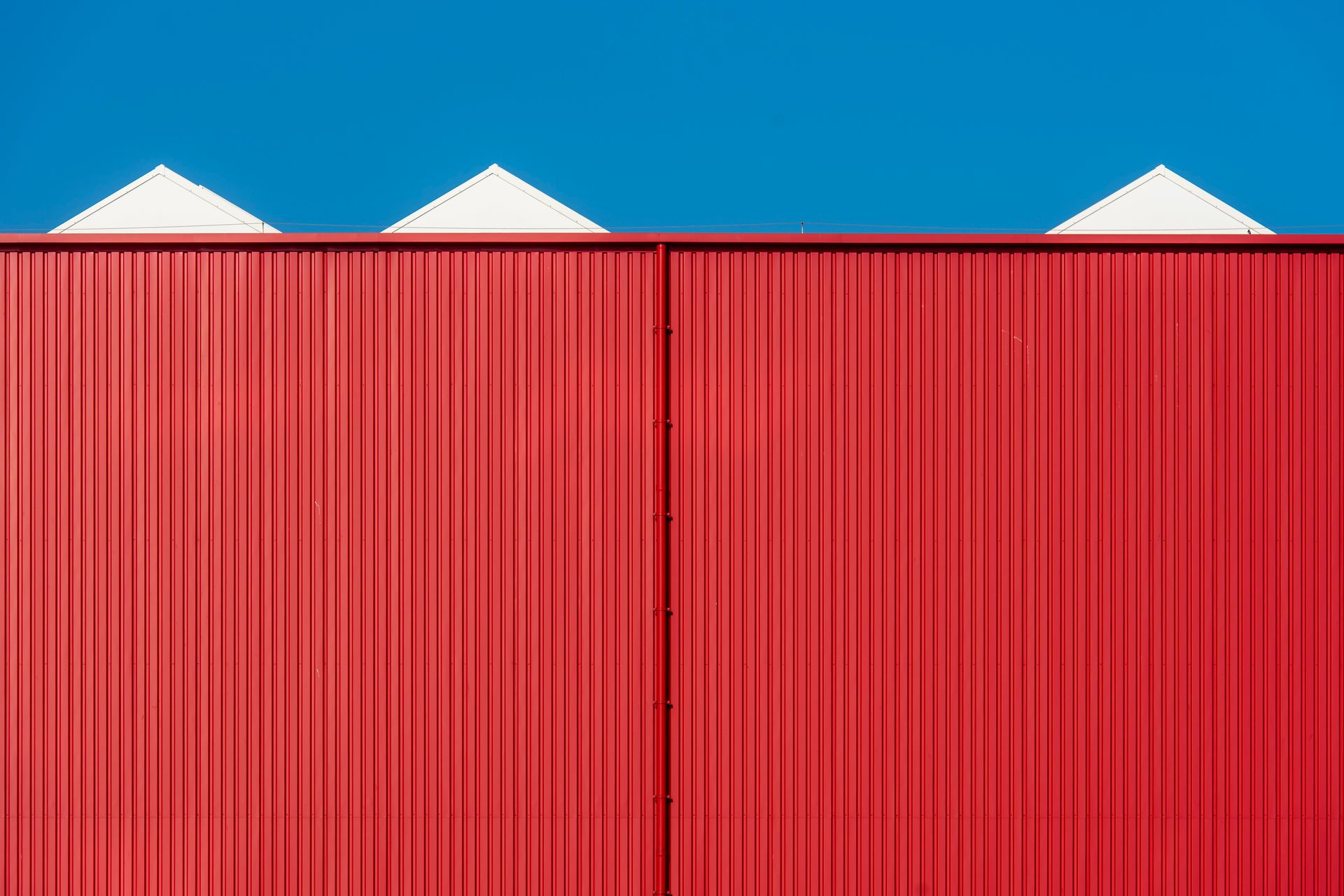 Minimalist photo of a red building facade against a bright blue sky, showcasing clean lines and vibrant colors.
