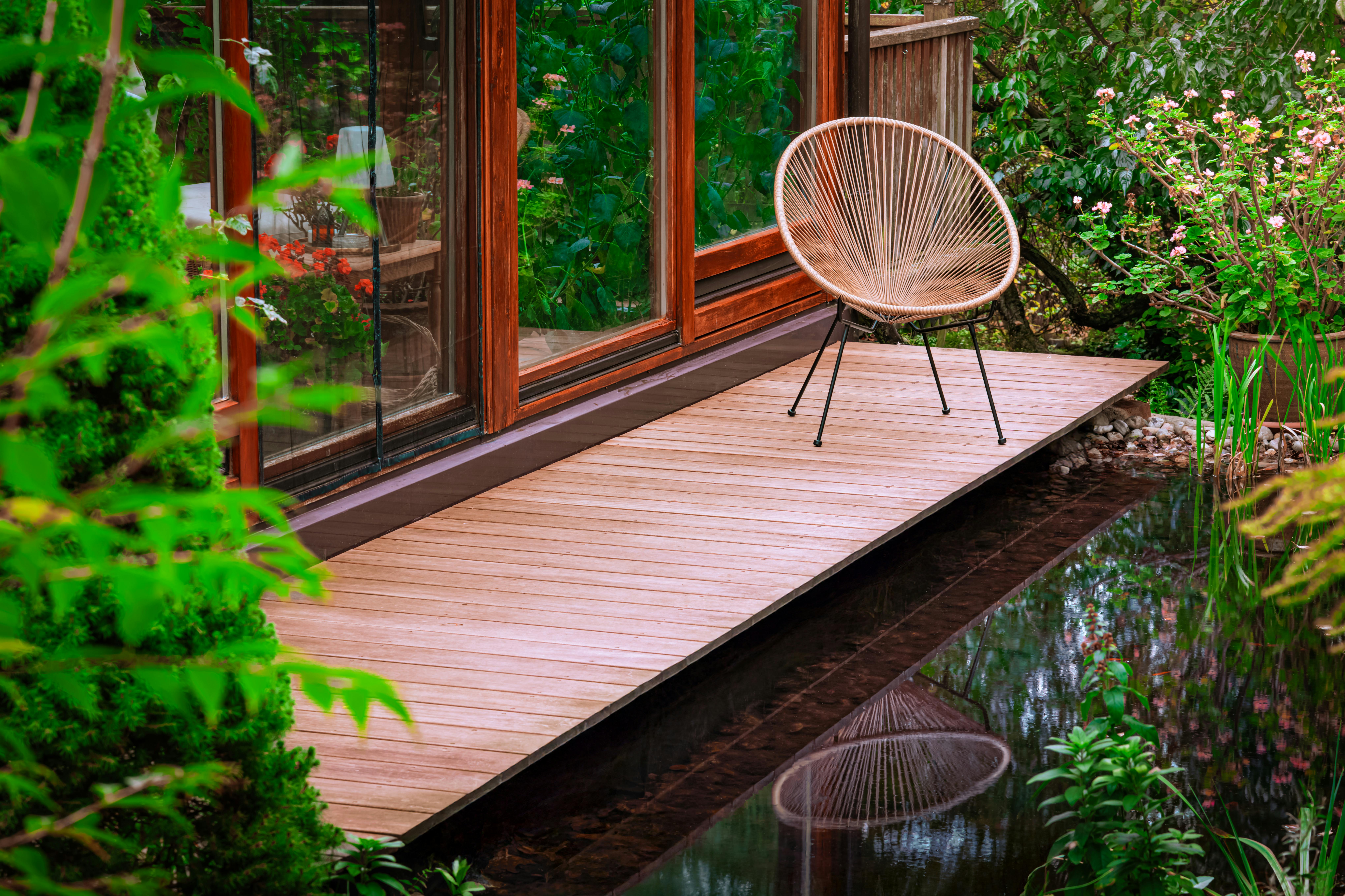 Serene garden setting with a modern chair on a wooden deck beside a reflective pond.